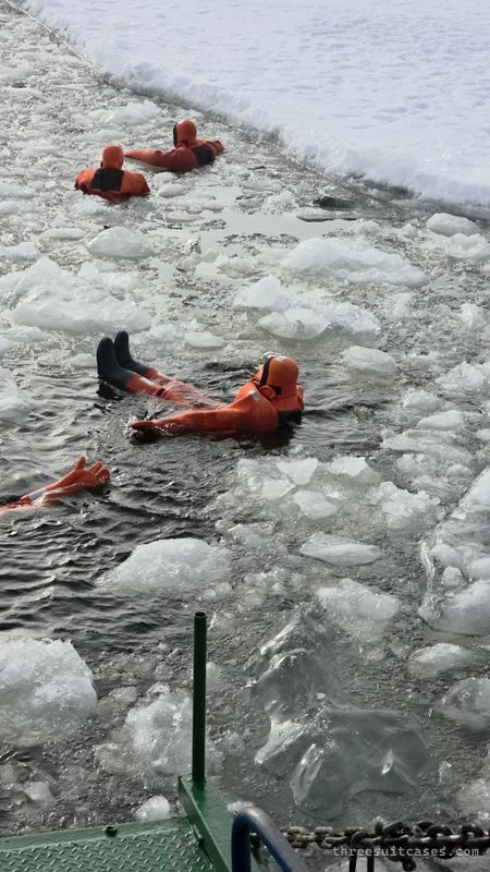 Adults floating among broken Baltic Sea ice in orange survival suits on the Polar Explorer cruise
